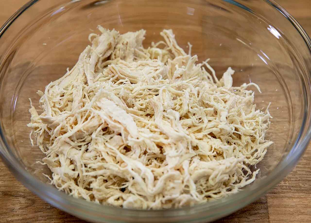 Pechuga de pollo cocida y desmenuzada servida en un tazón de vidrio transparente